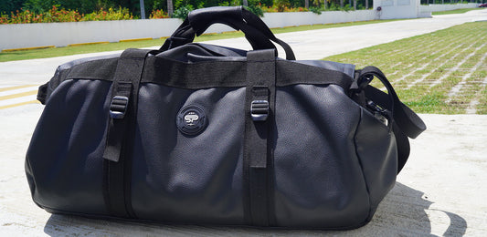 Large black duffel bag in the faux leather sitting on ground outside