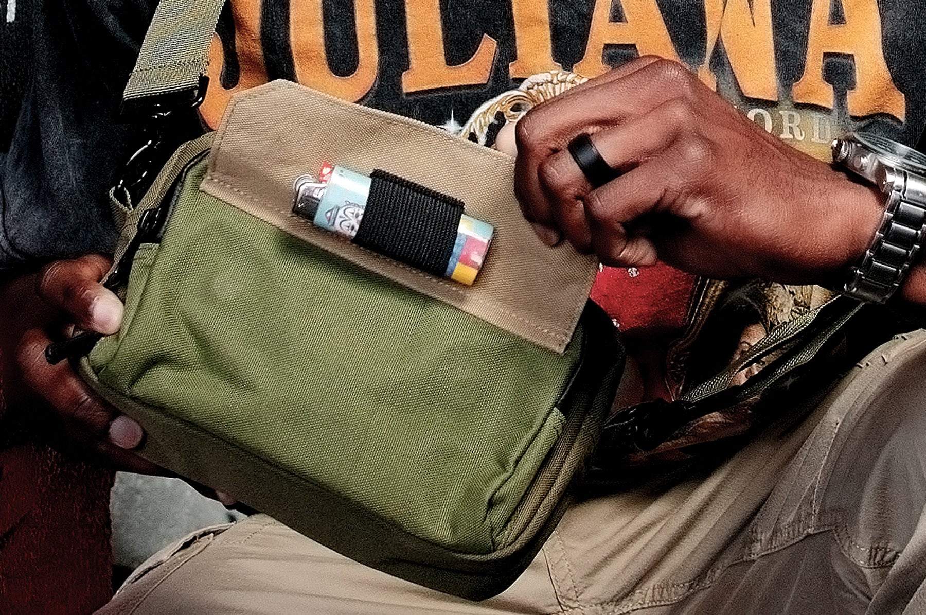 Man holding green and tan Flip bag exposing lighter holder underneath front flap