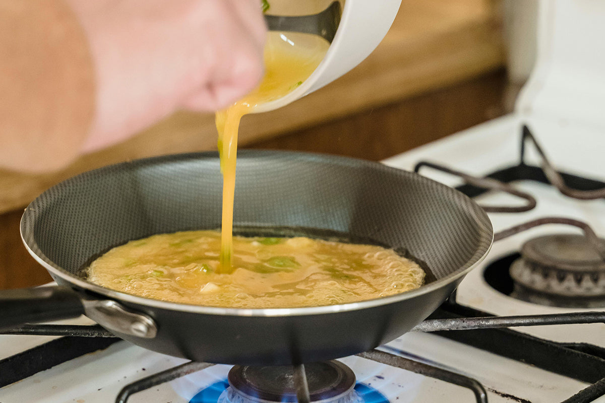 Person pouring egg mixture into a frying pan on a stove
