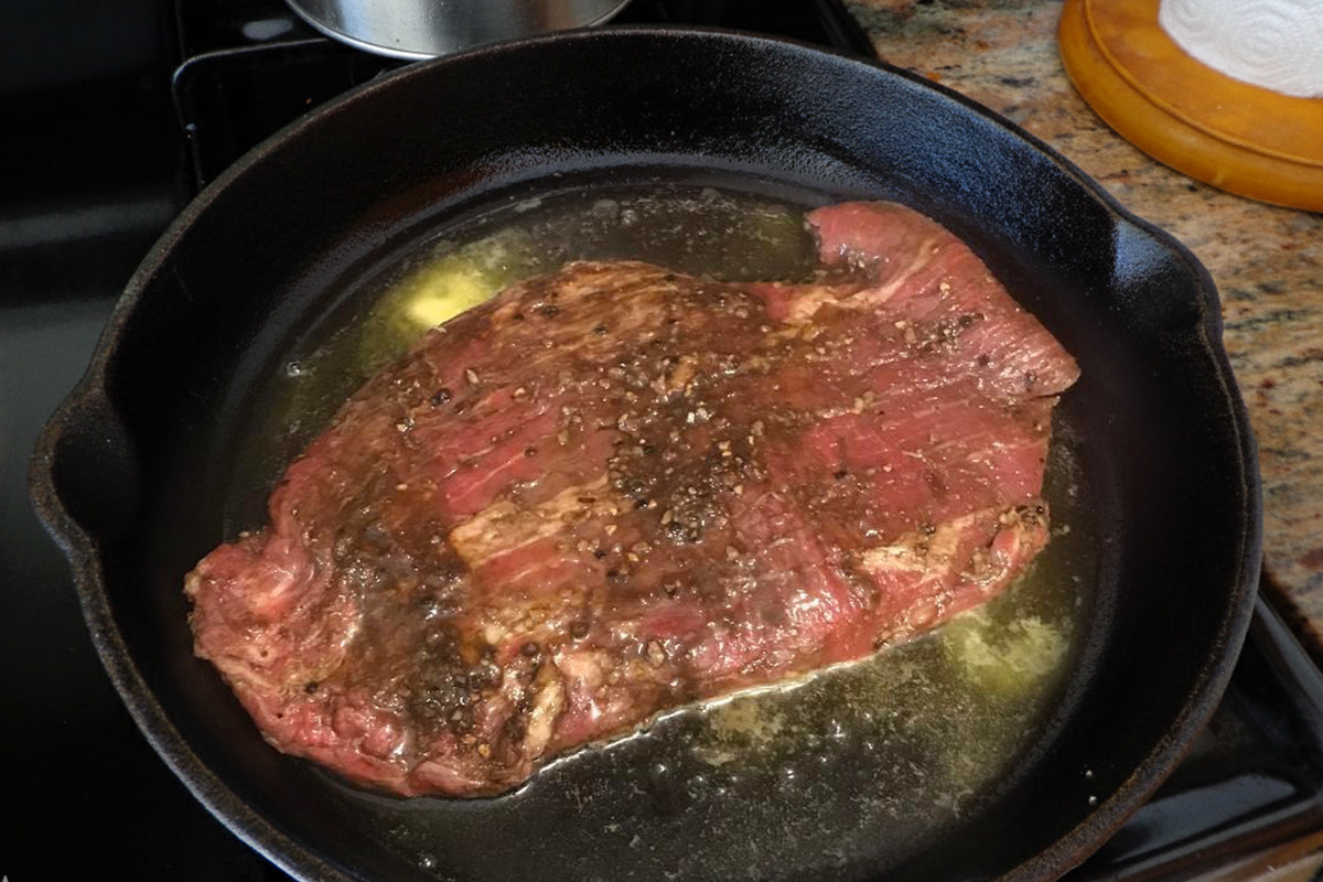 Steak being cooked in a cast iron skillet on a stovetop.