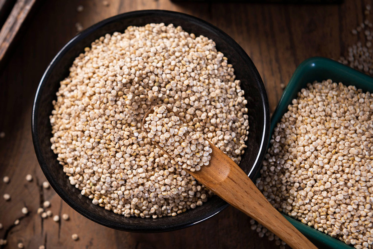 Quinoa in a black bowl with a wooden spoon on a wooden surface