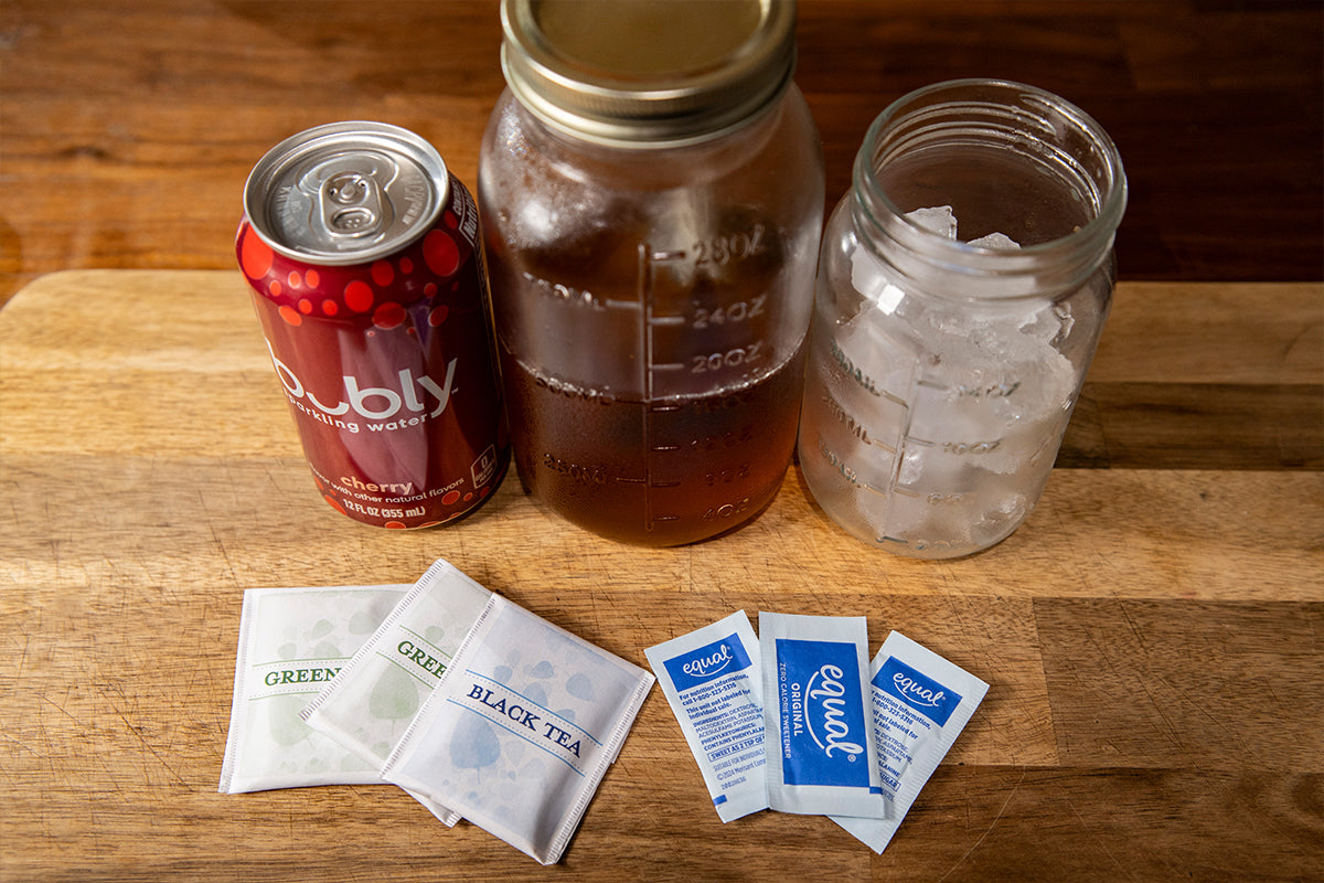 Bubly sparkling water can, jar of tea, jar of ice cubes, and tea bags on a wooden surface.
