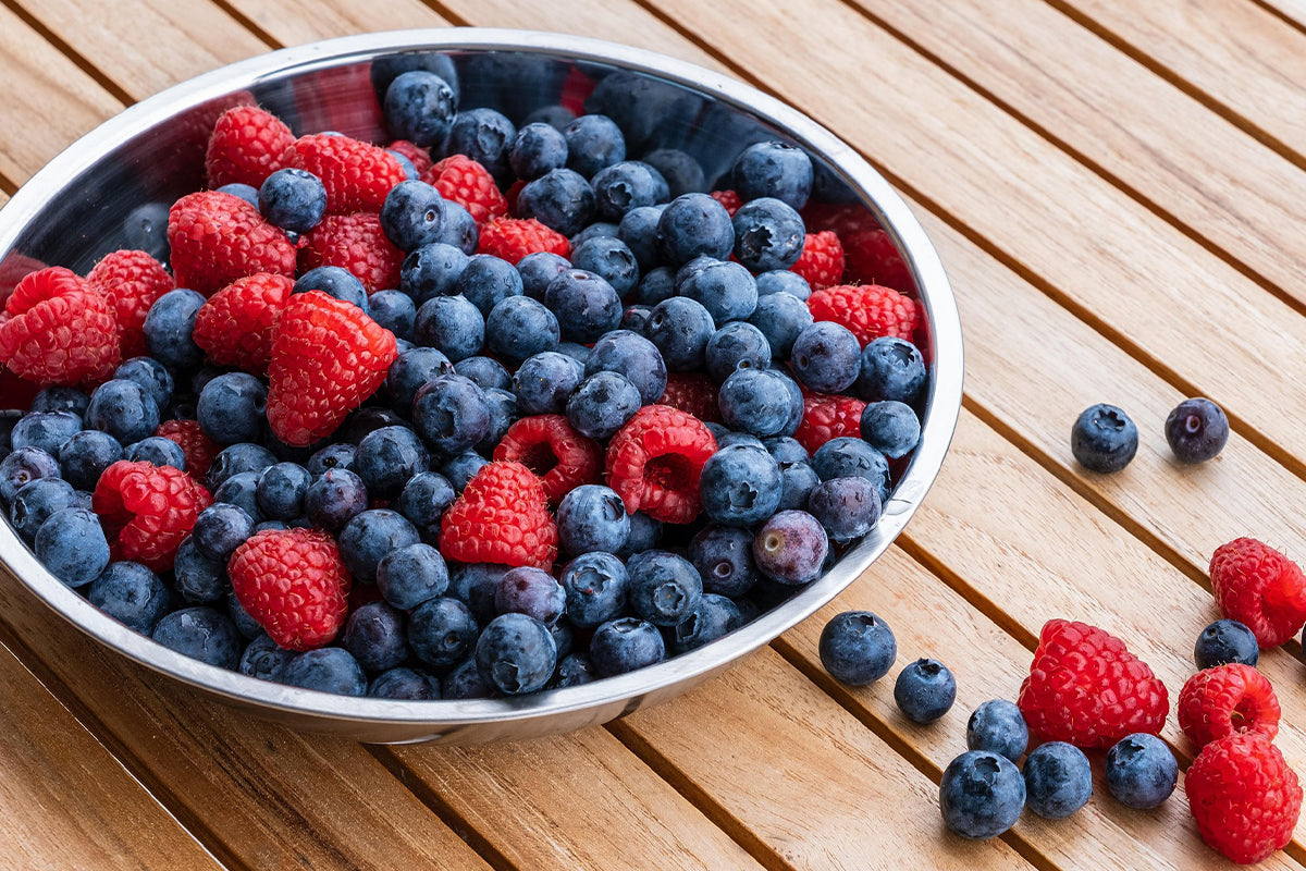 Bowl of mixed berries including blueberries and raspberries on a wooden surface.