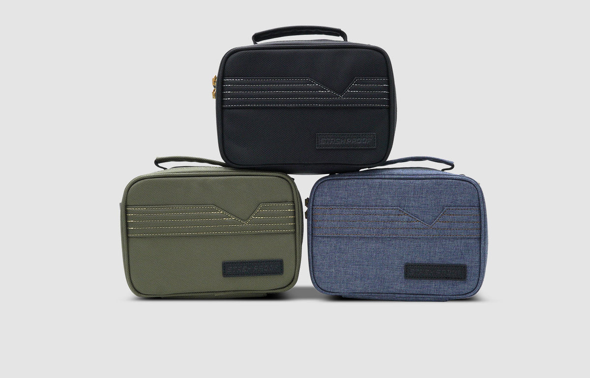 Three Stash Pack travel bags in black, green, and blue on a light gray background