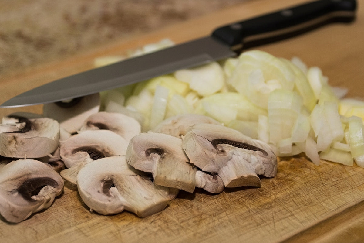 Sliced mushrooms and onions on a wooden cutting board with a knife.