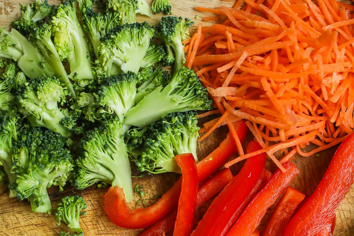 Broccoli, carrots, and red bell peppers on a wooden cutting board