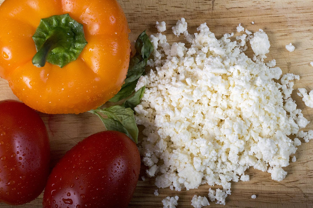 Orange bell pepper, red tomatoes, and crumbled white cheese on a wooden surface