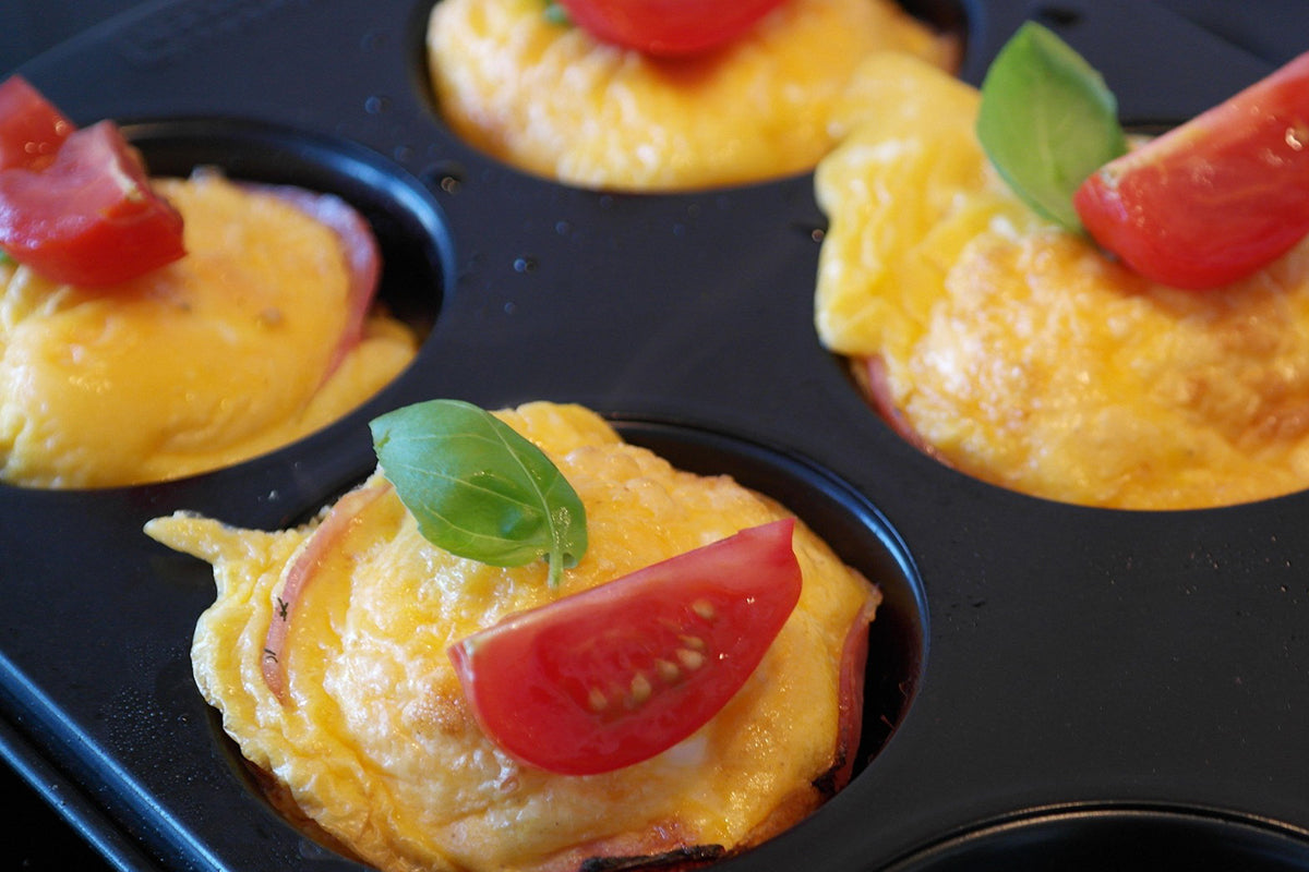 Mini omelette bites with tomatoes and basil in a muffin tin.