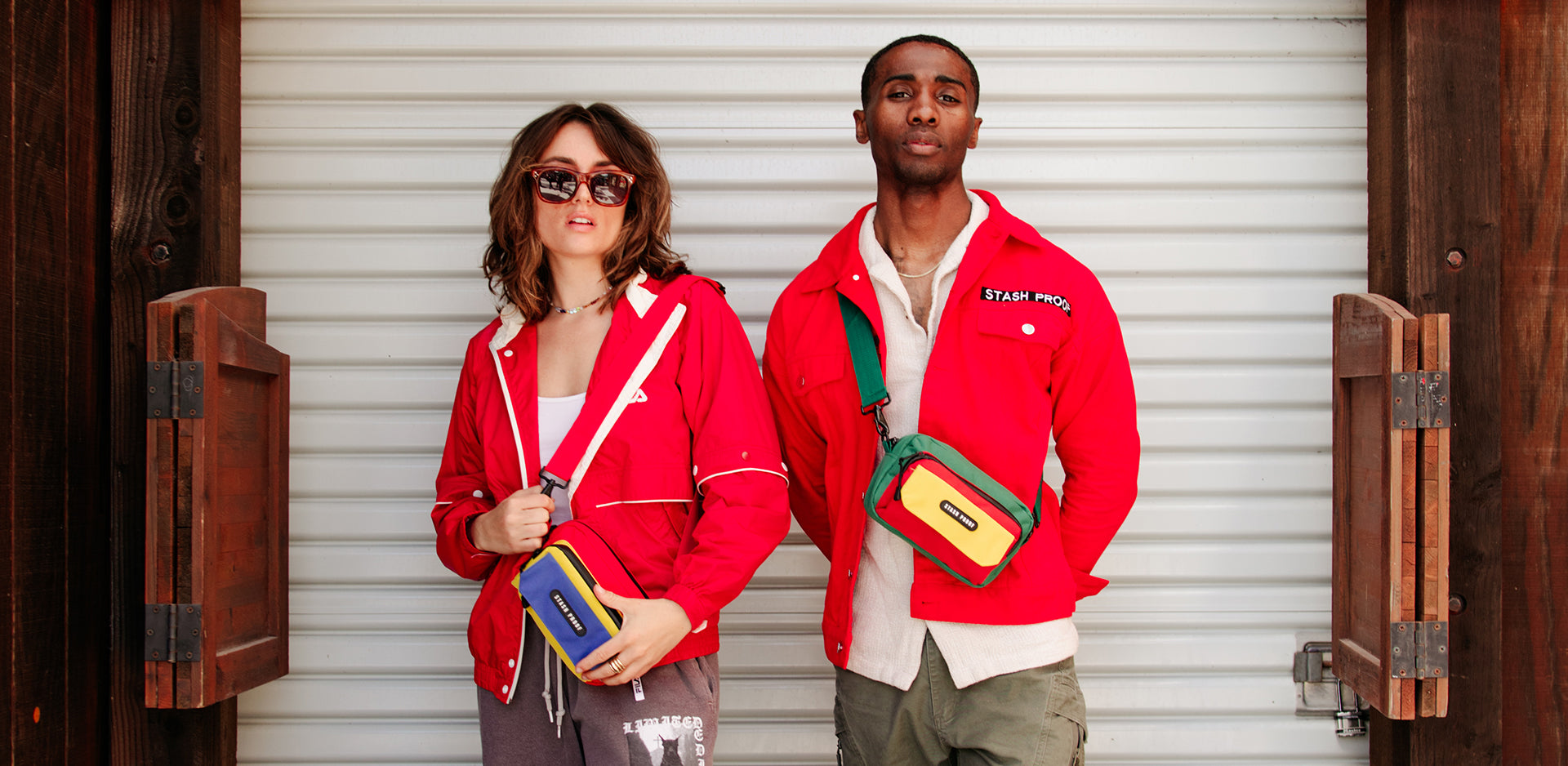 Two people wearing red jackets with stash proof label and carrying a red green and yellow rasta bag, standing in front of a wooden door.